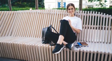 Gülümseyen beyaz yeniyetme kız dijital tablet ve haber okumak için 4G bağlantısı kullanarak caddede dinleniyor. Tablet üzerinden internet üzerinden iletişim kuran oldukça olumlu bin yıllık kadın.