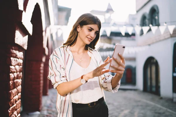 Carefree female blogger checking smartphone messages during online networking, happy Caucasian woman holding modern cellular device connecting to wireless internet for watching web vlog video