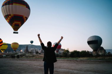 Kolları havada bir adamın dağlara inen renkli sıcak hava balonlarını izlemesi başarı ve yaşam başarısı ile heyecanlanır.