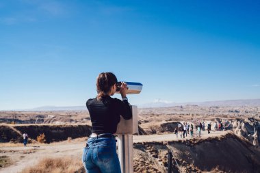 İnce figürlü genç bir kadının gözlem güvertesinde farklı turistlerle dolu bozuk para dürbünleriyle sonsuz çölleri keşfetmesi.