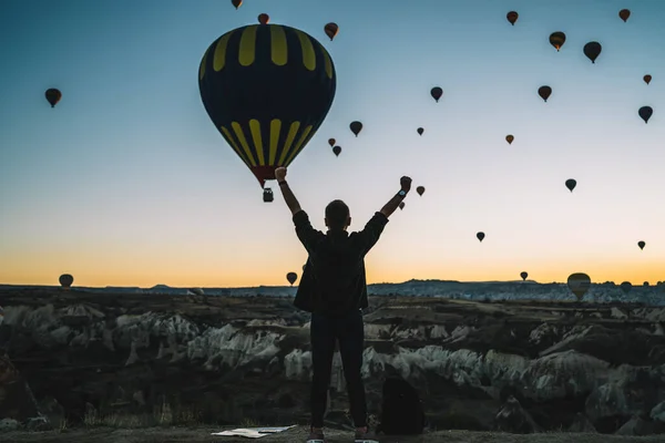 在丘陵地带 松懈的雄性站在悬崖边 手举着看日落时的气球的背景图 — 图库照片