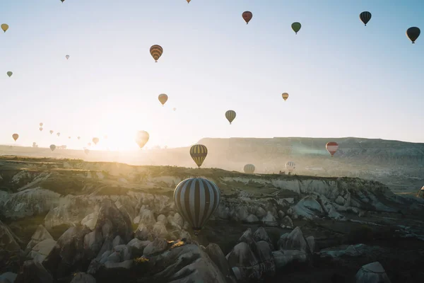 バックライト付きの空中ビューストライプの熱気球は 高地の夜明けと澄んだ空と地平線上に昇る太陽で互いに競争します — ストック写真