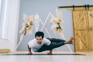 Konsantre olmuş bir adam spor minderinde sekiz açılı poziyon veriyor böylece modern stüdyoda yoga eğitimi sırasında kol ve bacak merkezini ve bilekleri güçlendiriyor.