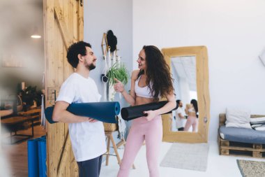 Modern stüdyoda ellerinde yoga minderleriyle durup birbirleriyle konuşurken gülümseyen neşeli, çok kültürlü arkadaşlar.