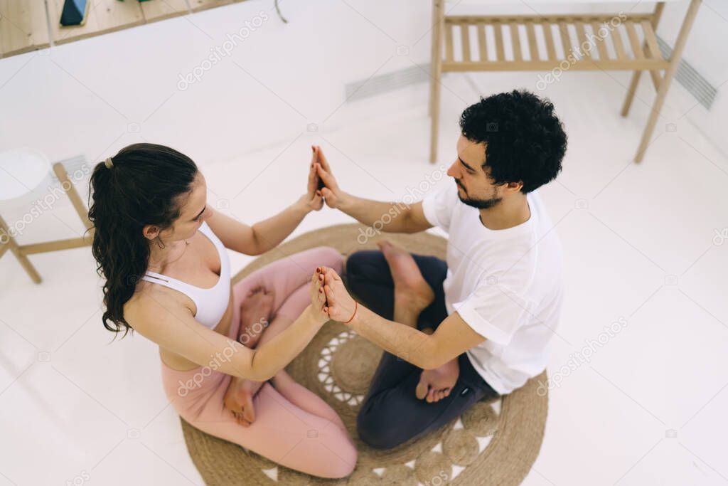 From above of young couple meditating together in lotus pose Padmasana sitting face to face on round mat on floor