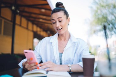 Gündüz vakti terasta mola verirken kafe masasında planlayıcıyla akıllı telefon kullanan ve kahve içen sıradan bir kadın.