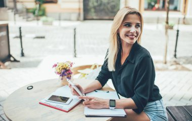 Modern dijital tablet kullanan başarılı bayan öğrenci kaldırım kafeteryasında öğrenme ve planlama yapıyor. Kafkasyalı, elinde teması olan hippi kız sokak kafesinde oturuyor ve gülümsüyor.