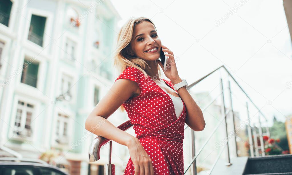 Half length portrait of charming woman smiling at camera while dialing international number for communicate about travel lifestyle, good looking female using roaming for talking via application