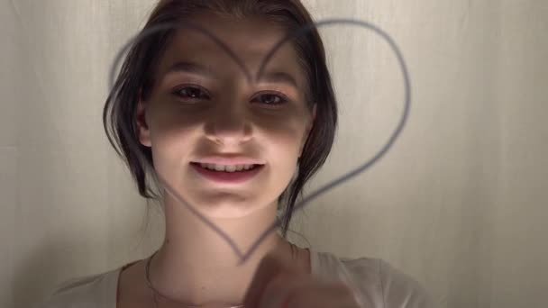 Привлекательная женщина рисует сердце на стеклянной доске, портрет лица крупным планом — стоковое видео