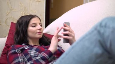 Cep telefonu kullanan, rahatlatıcı, rahat bir oturma odası atmosferi olan bir kadın.