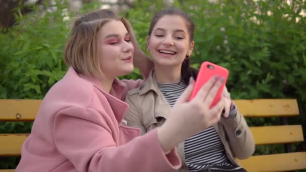 Két vonzó lány szelfit készít, barátok leszbikus pár sétál a parkban — Stock videók