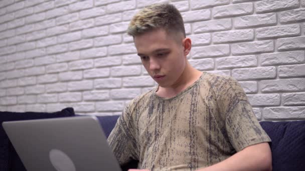 Fiatal férfi laptoppal, szabadúszó online dolgozik, távoktatás otthon — Stock videók
