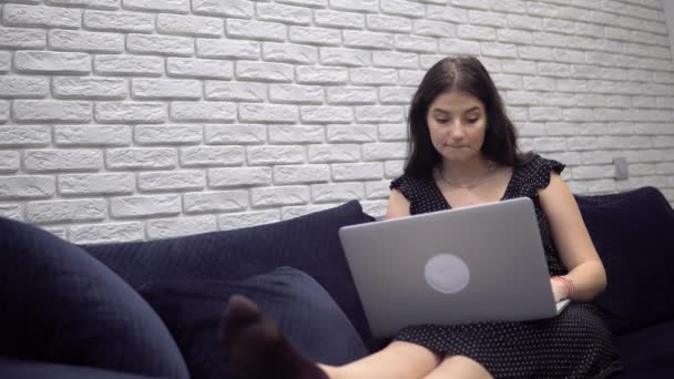 Mulher atraente usando laptop no sofá sofá, relaxando em casa, chatiing — Vídeo de Stock