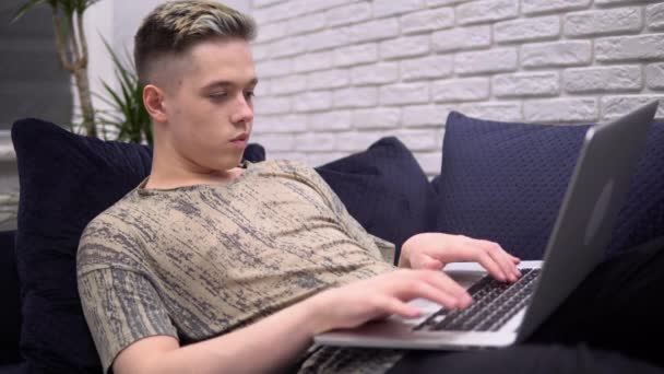 Homem digitando no teclado, usando laptop, relaxando no sofá, freelance, quarentena — Vídeo de Stock