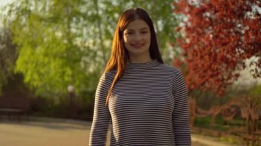 Mutlu kadın kameraya bakıyor, gülüyor, konuşuyor, gün batımında parkta konuşuyor.