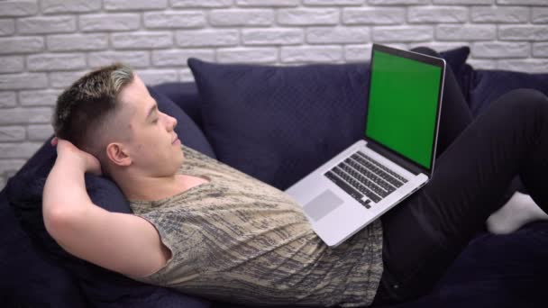Jonge student Man ontspannen op de bank, op zoek laptop groen scherm mockup — Stockvideo