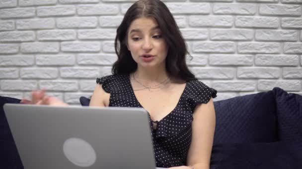 Çekici kadın görüntülü konuşma yapıyor, internette, evdeki kanepede dizüstü bilgisayar kullanıyor. — Stok video