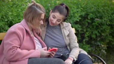 Genç bayan arkadaşlar cep telefonuna bakıyor, parkta yürüyor.