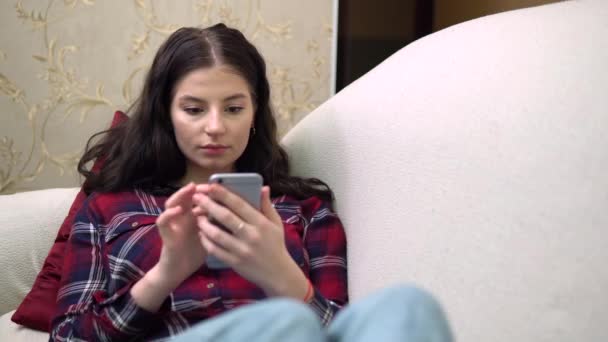 Mujer usando el teléfono móvil, riendo, relajante, acogedor ambiente de sala de estar en casa — Vídeo de stock