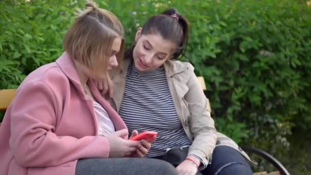 Jonge vrouwelijke vrienden kijken naar mobiele telefoon, wandelen in het park — Stockvideo