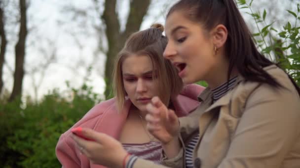 İki çekici mutlu kız telefon ekranına bakıp gülüyorlar, arkadaşlık konsepti. — Stok video