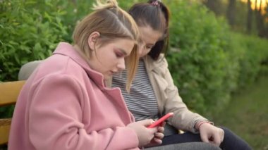 Genç bayan arkadaşlar cep telefonuna bakıyor, parkta yürüyor.
