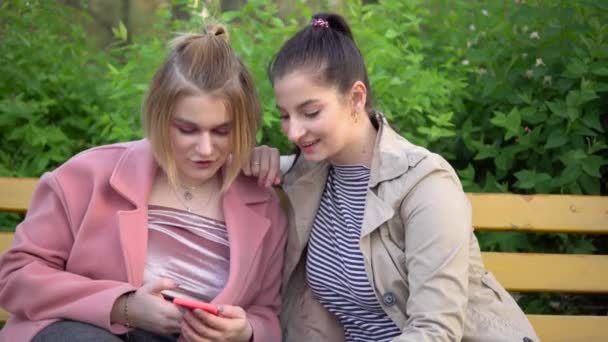 Молоді жінки друзі дивляться на мобільний телефон, ходять в парку — стокове відео
