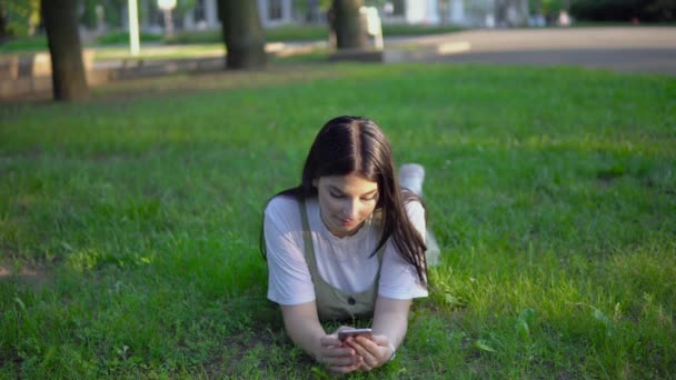 Atraktivní žena leží na trávě v parku pomocí smartphone, relaxační letní dovolená — Stock video