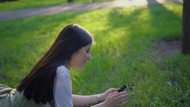 Aantrekkelijke vrouw ligt op gras in park gebruik smartphone, ontspannen zomervakantie — Stockvideo