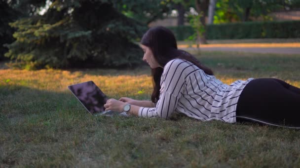 Nő a füvön a parkban laptop, szabadúszó távolság távmunka — Stock videók