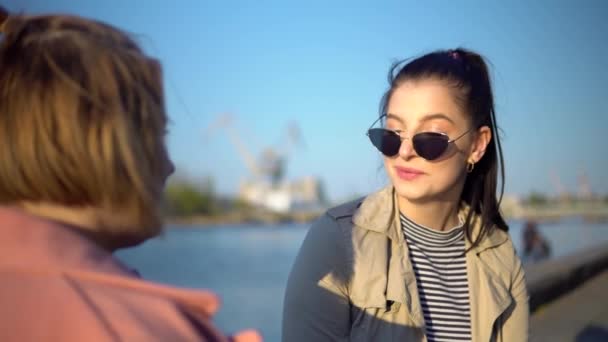 Молодая счастливая женщина разговаривает с другом, смеется, ходит по набережной — стоковое видео