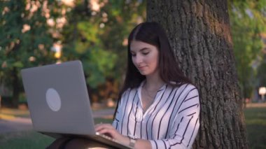 Parkta oturan çekici bir kadın, dizüstü bilgisayar kullanıyor, serbest çalışıyor.