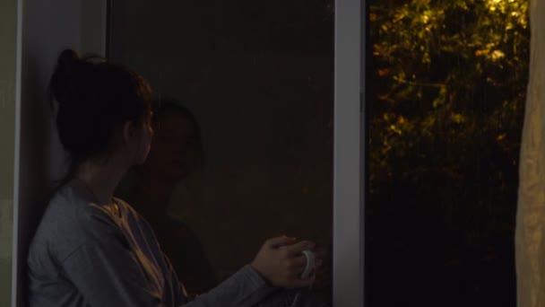 Woman with cup on windowsill looking on rain, relaxing, autumn cozy night — Stock Video