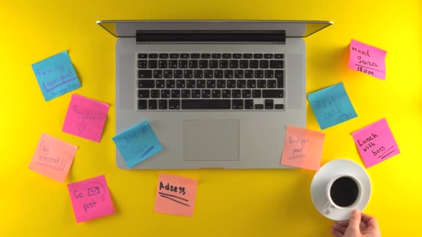 Milieu de travail avec post-it papiers sur bureau, ordinateur portable sur fond jaune, pause café — Video