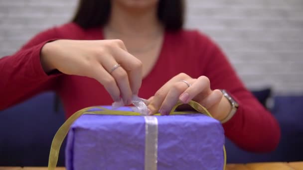 Kobieta przywiązuje wstążkę do prezentu, pakując prezent na wakacje sama — Wideo stockowe