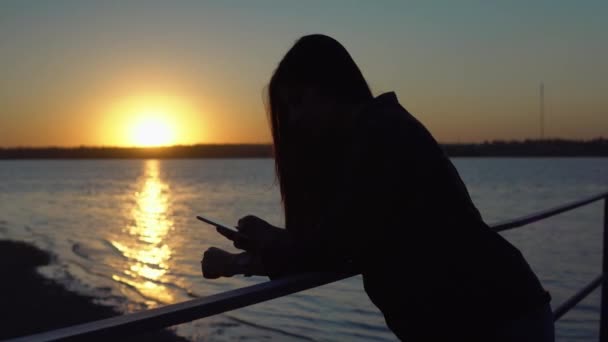 Kvinna går på piren, med mobiltelefon, svart kvinna siluett på solnedgången — Stockvideo