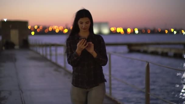 Kvinnan går nerför gatan kaj använder telefon texter rullar surfa på internet söka nyheter — Stockvideo