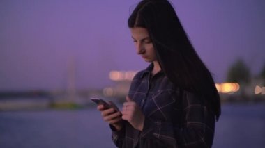 Rıhtımda elinde telefonla yürüyen bir kadın, gece sokakta cep telefonuyla mesajlaşan bir kadın.