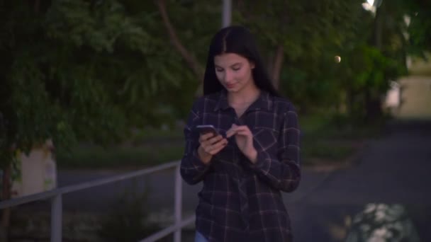 Woman walks down to the street uses phone texts surfs the internet search news — Stock Video