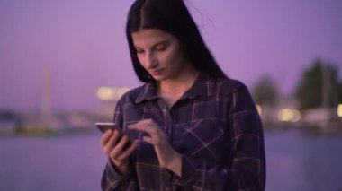 Çekici kadın sokakta, akşam yürüyüşünde, blogcu mesajlarında akıllı telefon kullanıyor.