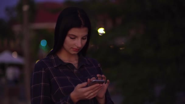 Mujer atractiva mirando la pantalla móvil, caminando por la noche y utilizando el teléfono inteligente — Vídeos de Stock