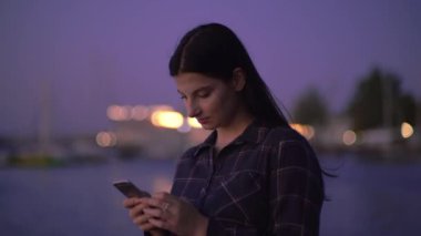 Smartphone 'da yazan bir kadın. Faiz ile birlikte. Gece sokakta, rıhtımın yanında.