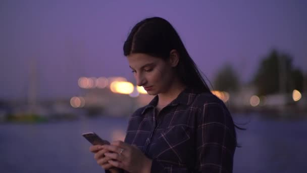 Γυναίκα πληκτρολογώντας στο Smartphone με τόκο, νύχτα με τα πόδια στο δρόμο, κοντά στην αποβάθρα — Αρχείο Βίντεο