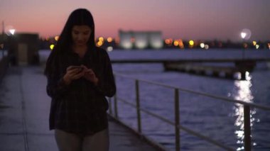 Rıhtımda cep telefonu kullanan, sokakta yürüyen ve telefonla mesajlaşan çekici bir kadın.
