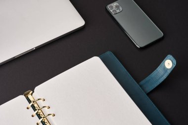 Açık yeşil el yapımı, altın kalemli, gri dizüstü bilgisayarı ve akıllı telefonu olan siyah masa.