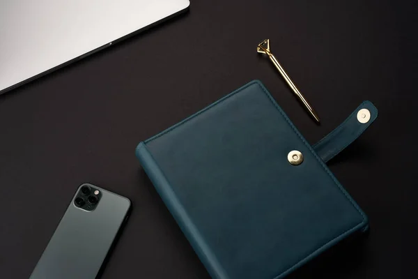 Black desk with green handmade notebooks, gray laptop and smartphone and gold pen — Stock Photo, Image