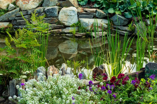 Красиво украшенный камнями и растениями искусственный водоем с отражением неба на воде. — стоковое фото