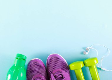 Eğitimciler, şişe, halter ve kulaklık üzerinde mavi arka plan - fitness ve spor kavramı