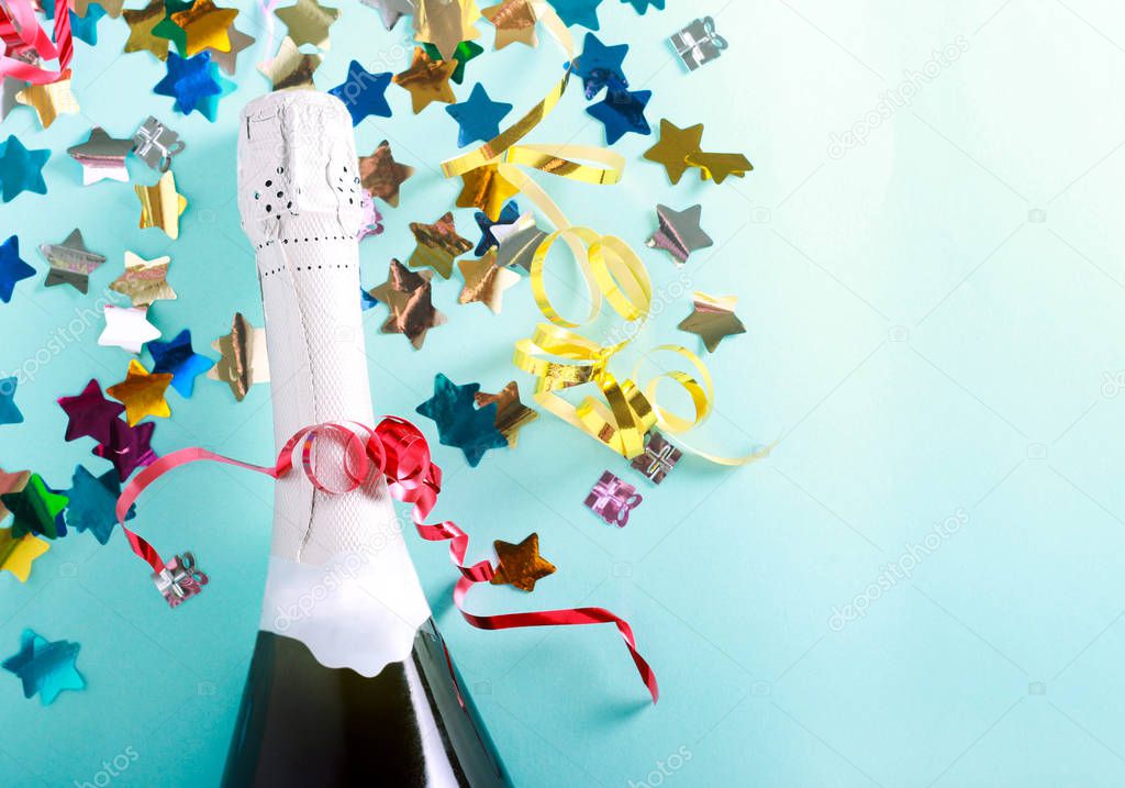 Party and celebration concept - bottle of Champaign and confetti over blue background