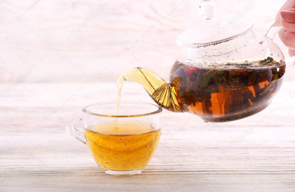 Pouring hot herbal tea in a cup over wooden background